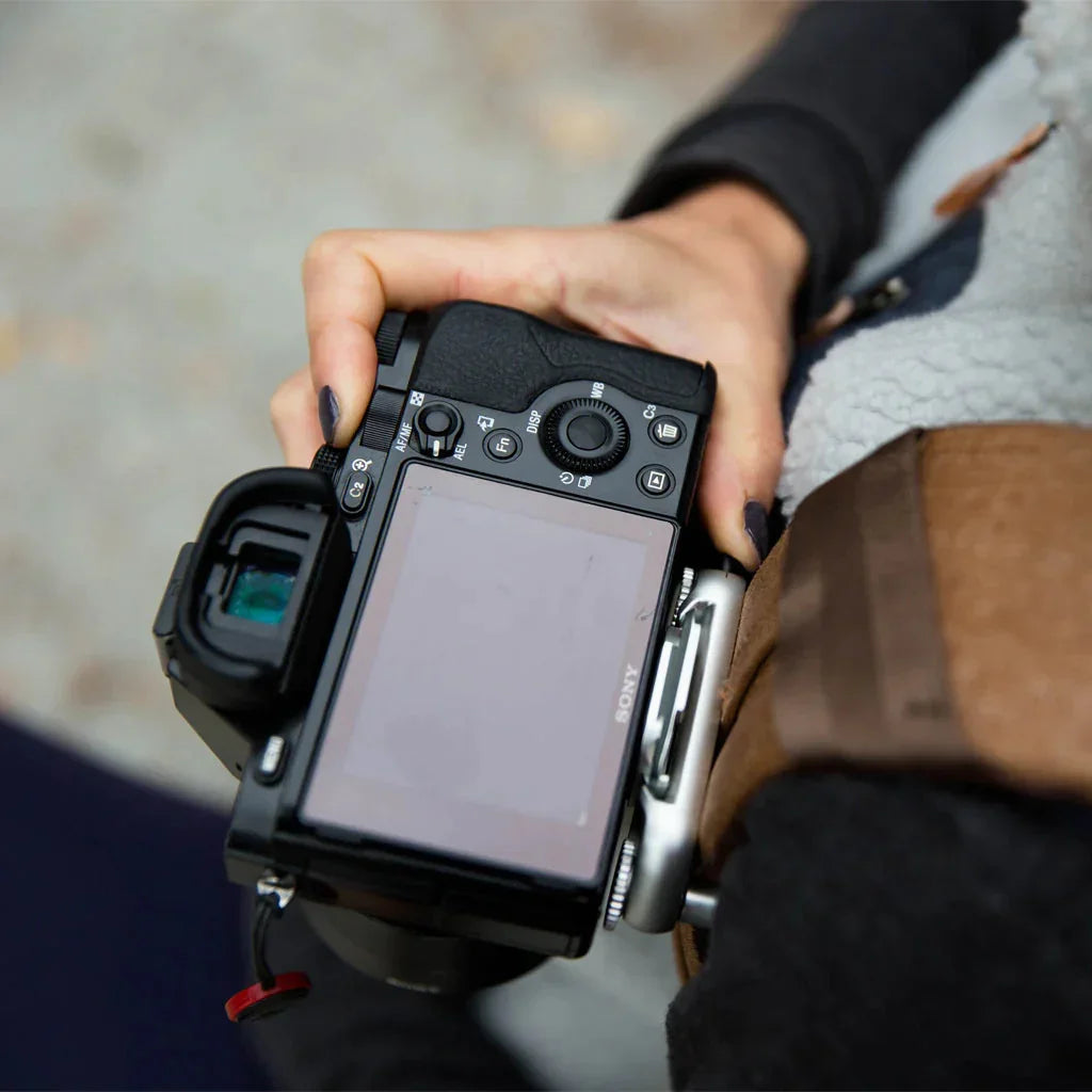 Osoba trzyma czarny aparat fotograficzny Sony z ekranem LCD, gotowy do robienia zdjęć.