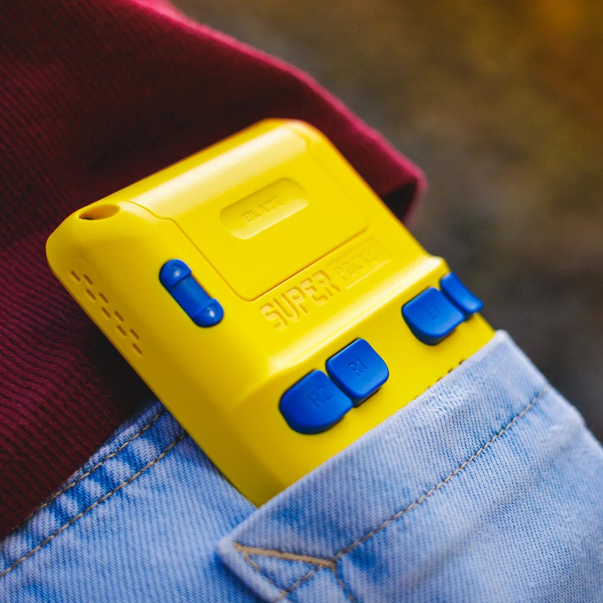 Żółty kontroler Super Pocket z niebieskimi przyciskami w kieszeni jeansów, idealny do gier mobilnych