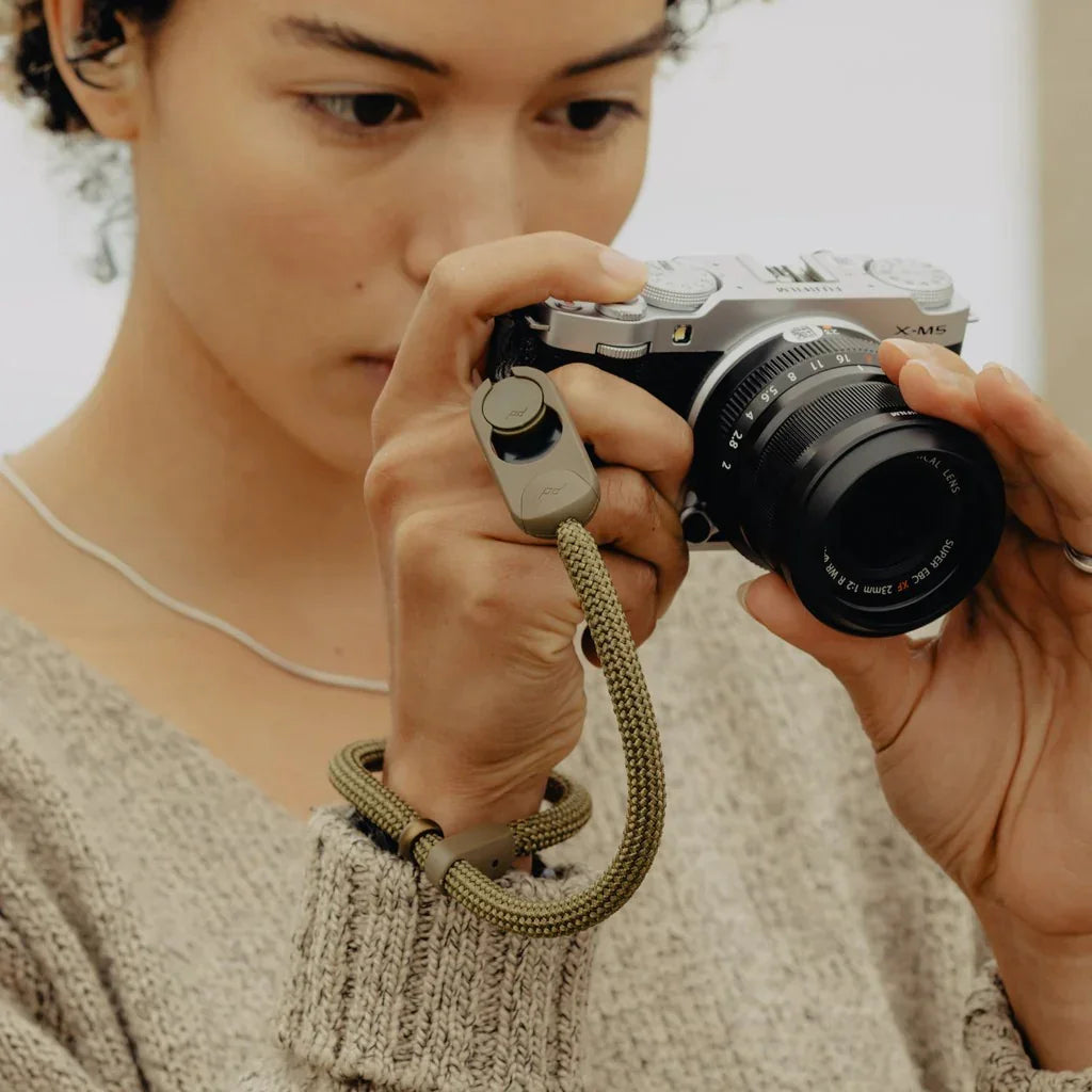 Kobieta trzyma aparat Fujifilm X-M5 z paskiem na nadgarstek, idealny akcesorium do fotografii i biura domowego