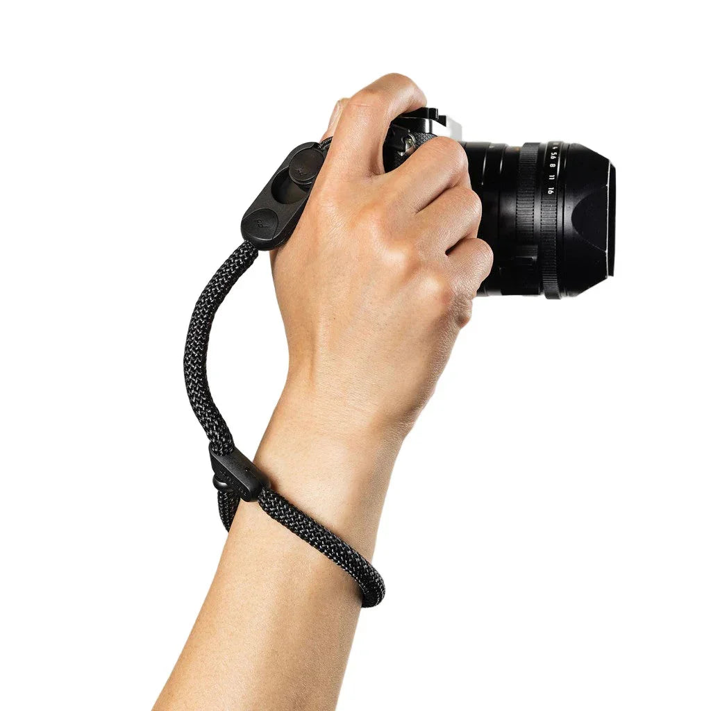 Czarny pasek na nadgarstek do aparatu fotograficznego, trzymany w dłoni, idealny dla fotografów